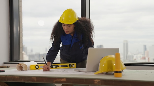 Arquitecta trabajadora con casco amarillo dibujando en el plano