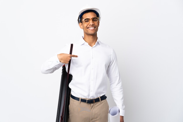 Arquitecto afroamericano hombre con casco y sosteniendo planos sobre pared blanca aislada orgulloso y satisfecho