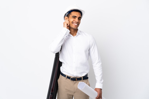 Arquitecto afroamericano hombre con casco y sosteniendo planos sobre pared blanca aislada _ riendo