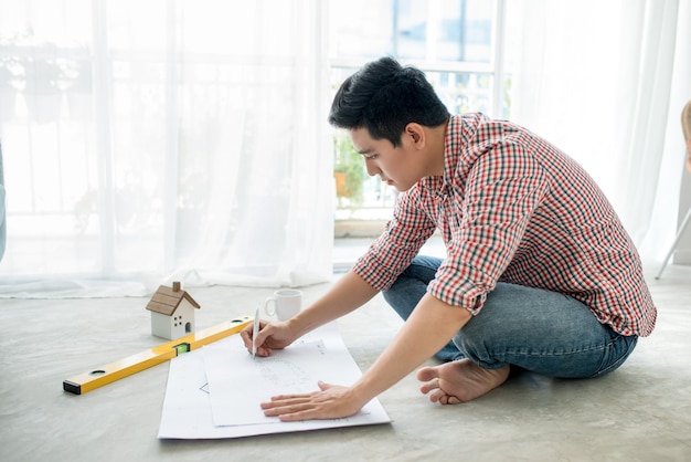 Arquitecto asiático masculino hermoso joven que trabaja en casa en el piso.