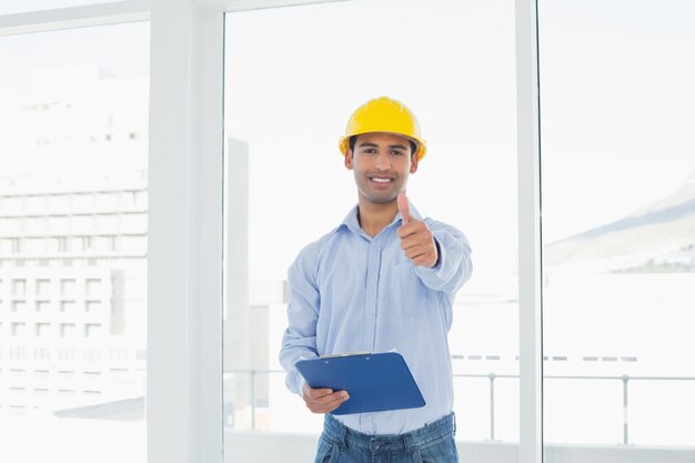 Foto arquitecto en casco con portapapeles gestos pulgares arriba en la oficina