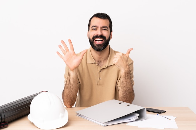 Arquitecto caucásico hombre con barba en una mesa contando seis con los dedos