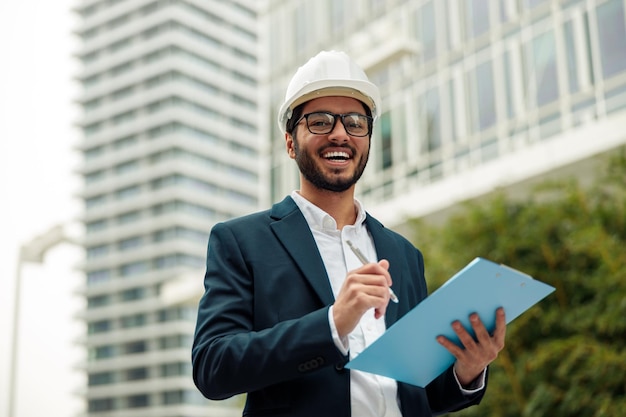 Arquitecto de construcción indio con traje y casco haciendo notas contra un edificio moderno