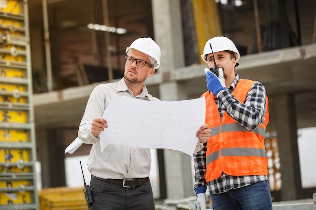 Arquitecto y desarrollador masculino con walkie talkie y planos en el sitio de construcción