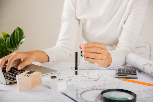 Arquitecto escribiendo el teclado de la computadora portátil para revisar el diseño de la casa antes de editar con la brújula