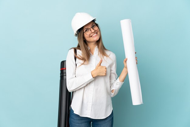 Arquitecto eslovaco chica sosteniendo planos aislado sobre fondo azul dando un pulgar hacia arriba gesto