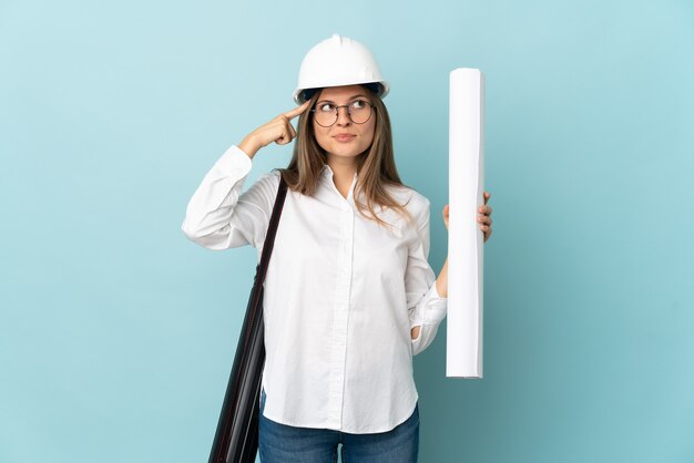 Foto arquitecto eslovaco chica sosteniendo planos aislados en la pared azul teniendo dudas y pensando