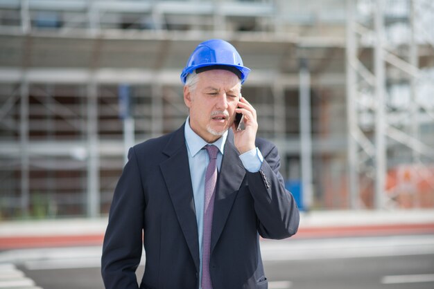 Arquitecto gerente hablando por el celular frente al sitio de construcción