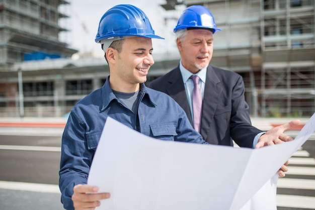 Arquitecto hablando con el administrador del sitio frente a un edificio de construcción