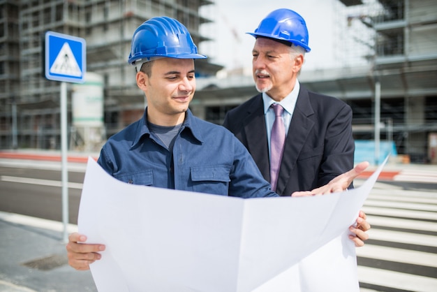 Arquitecto hablando con el administrador del sitio frente a un edificio de construcción