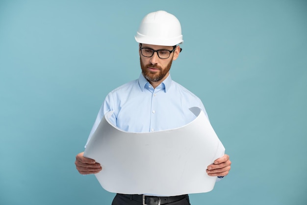 Arquitecto hombre con cara concentrada en casco de seguridad constructor mirando los planos sobre fondo aislado Concepto de ingeniero