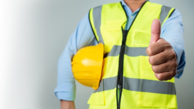 Arquitecto ingeniero civil de pie sosteniendo un casco de seguridad sobre un fondo gris