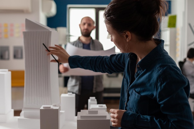 Foto arquitecto inspeccionando el diseño de edificios futuristas de rascacielos con un ingeniero colega que tiene planos. arquitectos haciendo trabajo en equipo en el escritorio con maqueta de espuma blanca del proyecto de construcción.