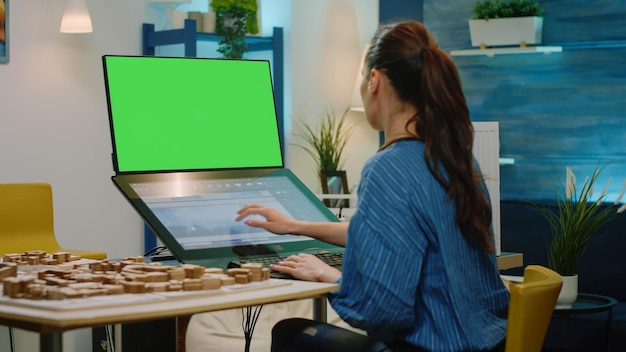 Arquitecto mirando la pantalla verde horizontal para construir un modelo en una computadora con pantalla táctil. Mujer ingeniera que trabaja con clave de croma con plantilla aislada y fondo de maqueta para el desarrollo