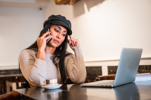 Arquitecto morena latina haciendo una llamada de trabajo con una computadora portátil desde una cafetería