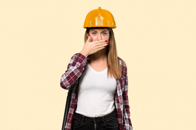 Arquitecto mujer cubriendo la boca con las manos para decir algo inapropiado sobre pared amarilla aislada