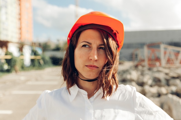 Arquitecto de la mujer hermosa joven en camisa blanca y casco que sostiene un tablero del tirón. mujer con casco en un sitio de construcción en casa.