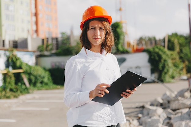 Arquitecto de la mujer hermosa joven en camisa blanca y casco que sostiene un tablero del tirón. mujer con casco en un sitio de construcción en casa.