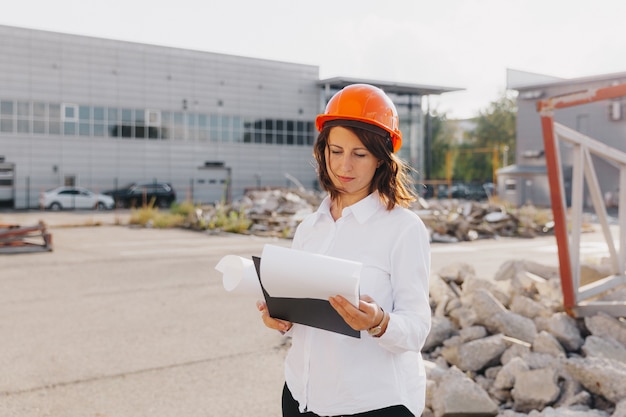 Arquitecto de la mujer hermosa joven en camisa blanca y casco que sostiene un tablero del tirón. mujer con casco en un sitio de construcción en casa.