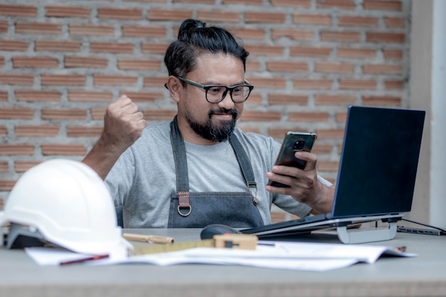 Arquitecto o ingeniero masculino que trabaja en casa dibujando el teléfono bilis del proyecto de construcción en el escritorio de trabajo