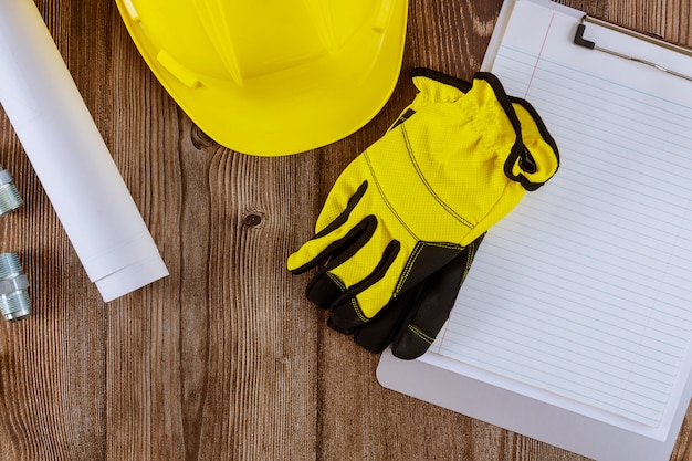 Arquitecto o ingeniero que trabaja en modo de arquitectura de planos en guantes de protección de construcción de oficinas en casco de seguridad amarillo