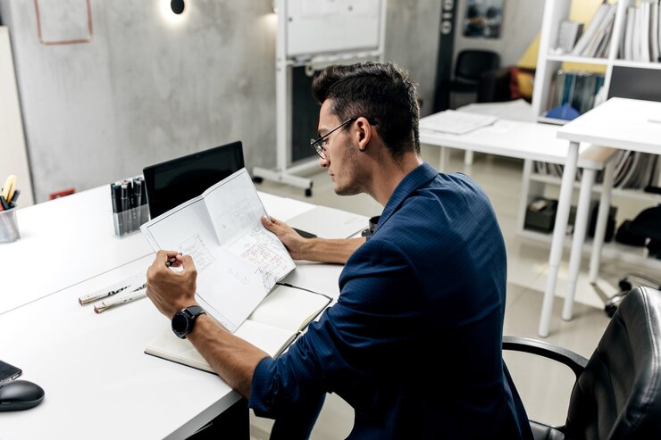 Foto arquitecto de pelo oscuro con estilo con gafas y una chaqueta azul está trabajando con documentos en el escritorio de la oficina.