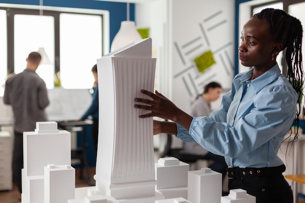 Arquitecto de pie en el escritorio con maqueta de espuma blanca del proyecto de construcción en la oficina de arquitectura moderna. Ingeniero inspeccionando el diseño futurista de edificios 3d de rascacielos.