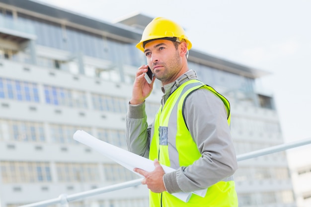 Arquitecto con planos usando teléfono móvil contra edificio