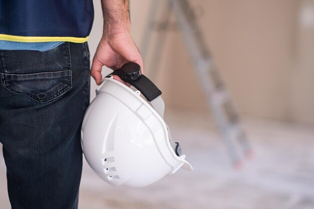 Arquitecto profesional con casco blanco en la mano parado contra la escalera