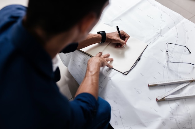 Arquitecto profesional toma notas en un cuaderno sobre una mesa con un dibujo y una regla.