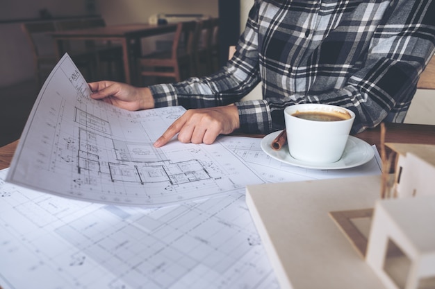 Foto un arquitecto que trabaja en un modelo de arquitectura con papel de dibujo de tienda y taza de café