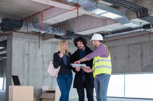 Foto arquitecto que usa una tableta mientras muestra los planes de diseño de la casa a una pareja joven en el sitio de construcción