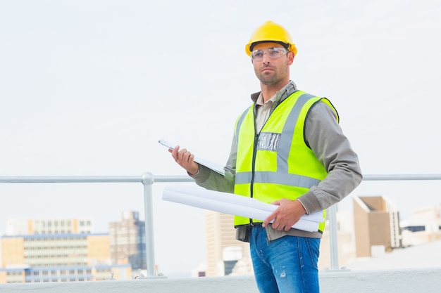 Arquitecto sosteniendo planos y portapapeles al aire libre