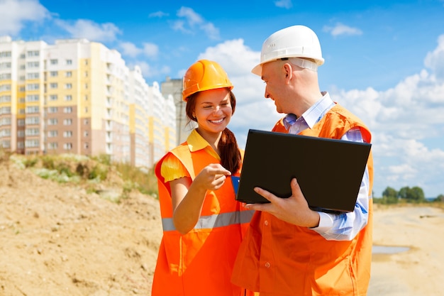 Arquitecto y trabajador de la construcción femenina mirando portátil juntos contra la construcción