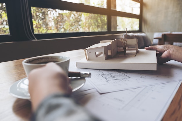 Foto arquitecto trabajando en un modelo de arquitectura con papel de dibujo de la tienda mientras bebe café