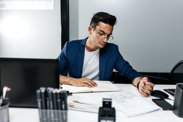 El arquitecto vestido con una chaqueta azul oscuro trabaja con documentos en el escritorio de la oficina.