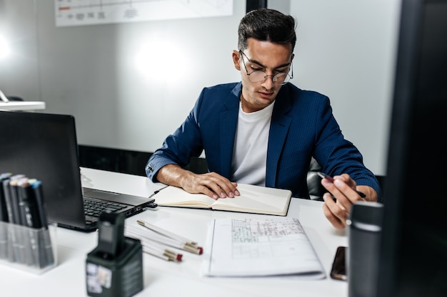 El arquitecto vestido con una chaqueta azul oscuro trabaja con documentos en el escritorio de la oficina.