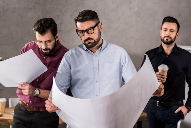 Arquitectos caucásicos guapos con planos en la oficina