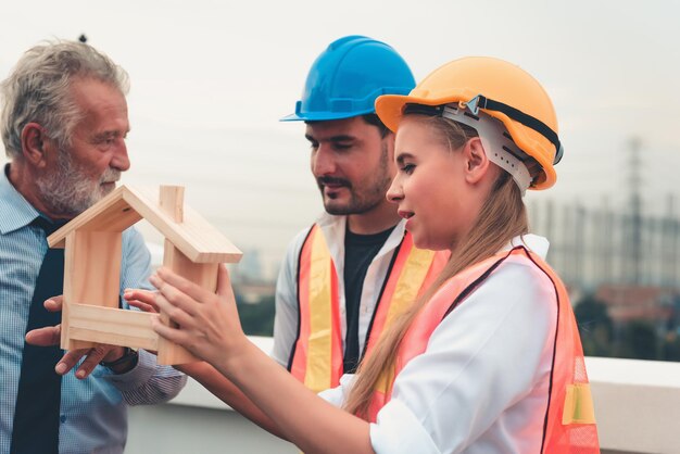 Foto arquitectos sosteniendo una casa modelo mientras están de pie en la terraza de la construcción