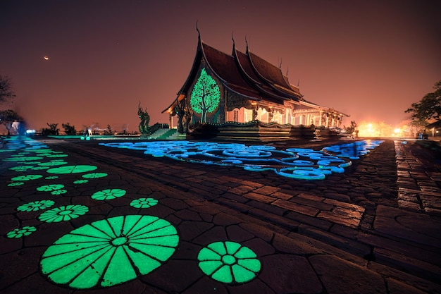 Arquitectura del templo de la iglesia con árbol bodhi que brilla intensamente y pintura de loto fluorescente en el suelo en Wat Sirindhorn Wararam o Wat Phu Prao