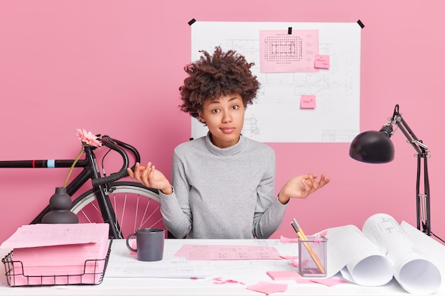 Foto arquiteta hesitante e talentosa abre as mãos em poses confusas na área de trabalho não sabe como melhorar os esboços de design