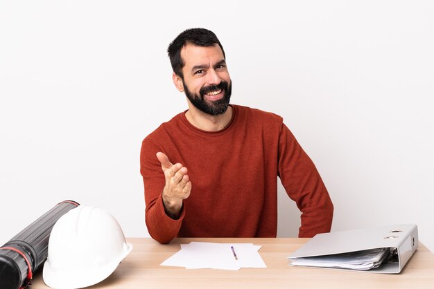 Arquiteto caucasiano com barba em uma mesa apertando as mãos para fechar um bom negócio.