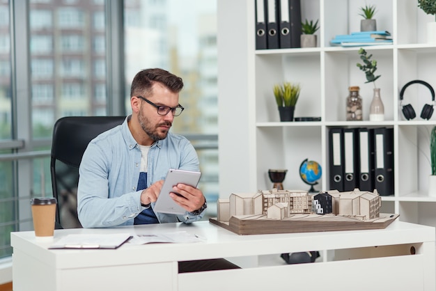 arquiteto experiente em escritório inspeciona o projeto de um complexo residencial e faz cálculos usando um tablet PC.