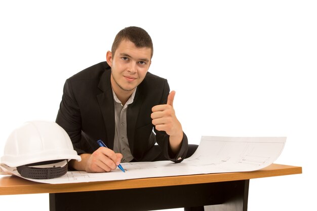 Arquiteto fazendo um gesto de sucesso com o polegar para cima enquanto se senta em uma mesa trabalhando em um plano de construção
