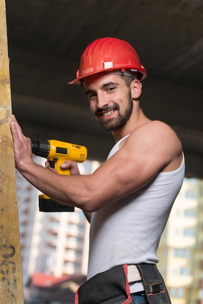 Foto arquiteto masculino bem sucedido em um canteiro de obras tentando perfurar uma grande prancha de madeira