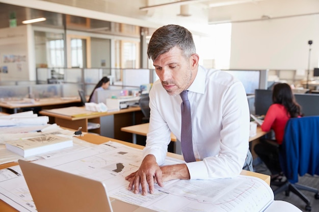 Arquiteto masculino de meia idade estudando planos em seu escritório