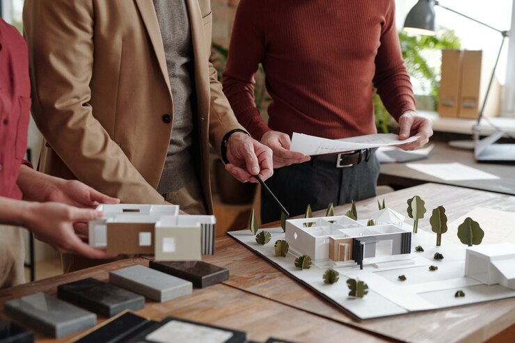Foto arquiteto masculino maduro com lápis apontando para o modelo da nova casa, enquanto seus jovens colegas segurando um papel com desenho e parte do layout