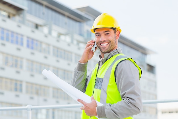 Arquiteto masculino sorridente com planos falando no celular