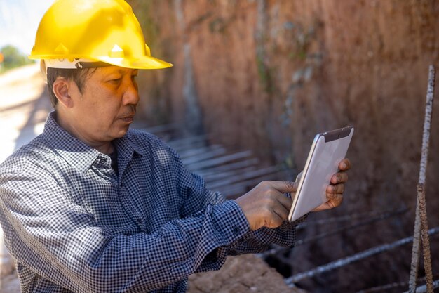 Arquiteto ou engenheiro civil com capacete de segurança no canteiro de obras, verificando a programação no computador tablet