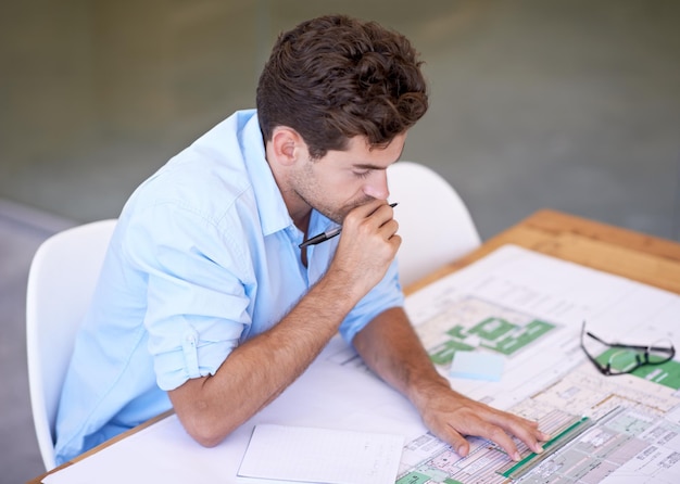 Arquiteto pensando ou homem no escritório com blueprint brainstorming e leitura de papel para projeto de construção Engenheiro designer ou desenvolvedor criativo na mesa com plano de piso para remodelação atualização